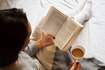 beautiful brunette girl reading book and drinking coffee in bed in the mornin