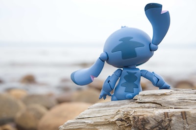 A nendoroid of Stitch from Lilo & Stitch. He sits on a log by the lake.
